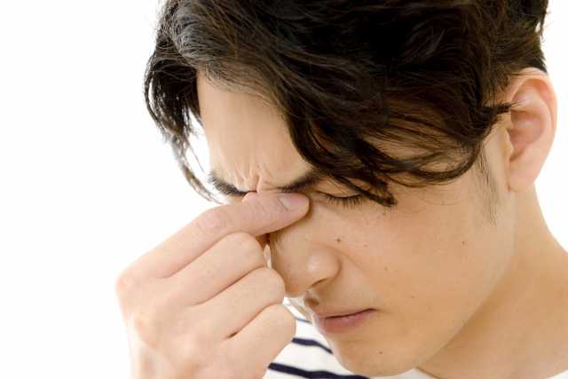 目頭を押さえて顔をしかめる男性