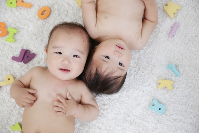 おもちゃに囲まれて並んで寝転ぶ双子の赤ちゃん