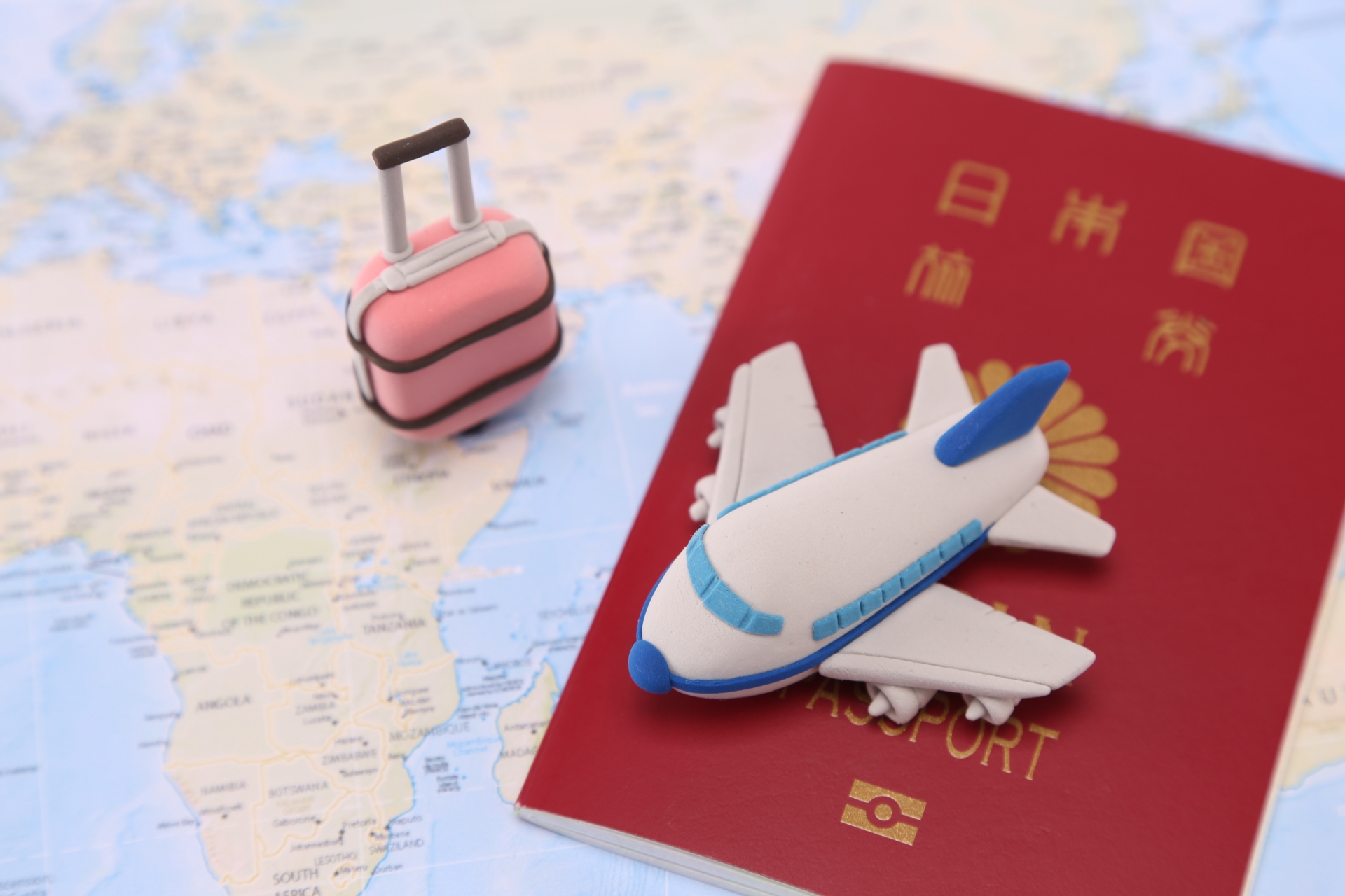 世界地図の上に置いたパスポートと飛行機とスーツケースの模型