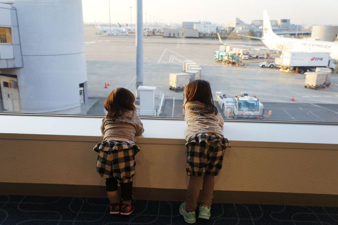 空港の窓から駐機場の飛行機をながめる子ども2人