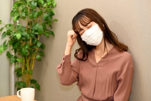 マスクをして体調が悪そうに座る女性