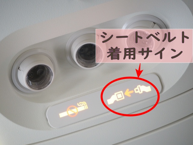 機内の座席上にあるシートベルト着用サインを赤い丸で示した写真