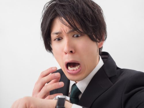 腕時計を見て慌てるスーツ姿の男性