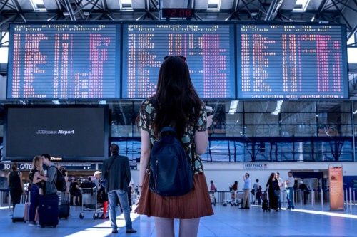 空港の大きな発着案内表示を見上げる女性の後ろ姿