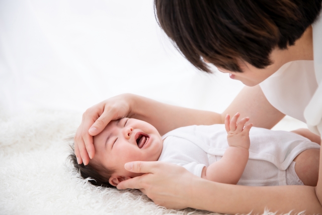 泣いている赤ちゃんの額に手を当てる大人