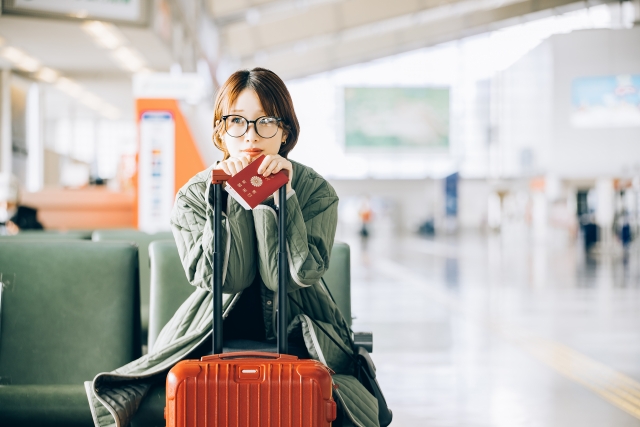 空港の椅子でスーツケースにもたれて待つ女性