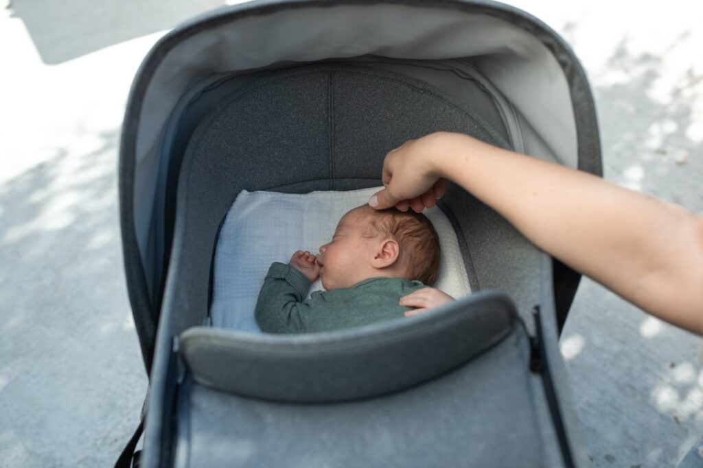 ベビーカーで眠る赤ちゃんに手を伸ばす大人