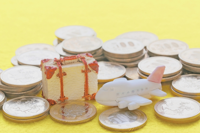 各国の硬貨に囲まれた飛行機とスーツケースの模型