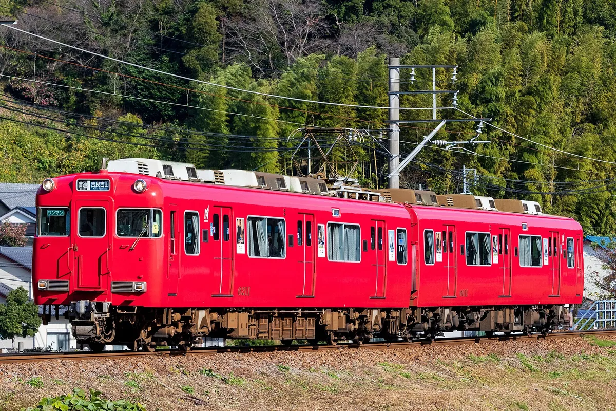山と竹林を背景に線路を走る名鉄電車の赤い車両の写真