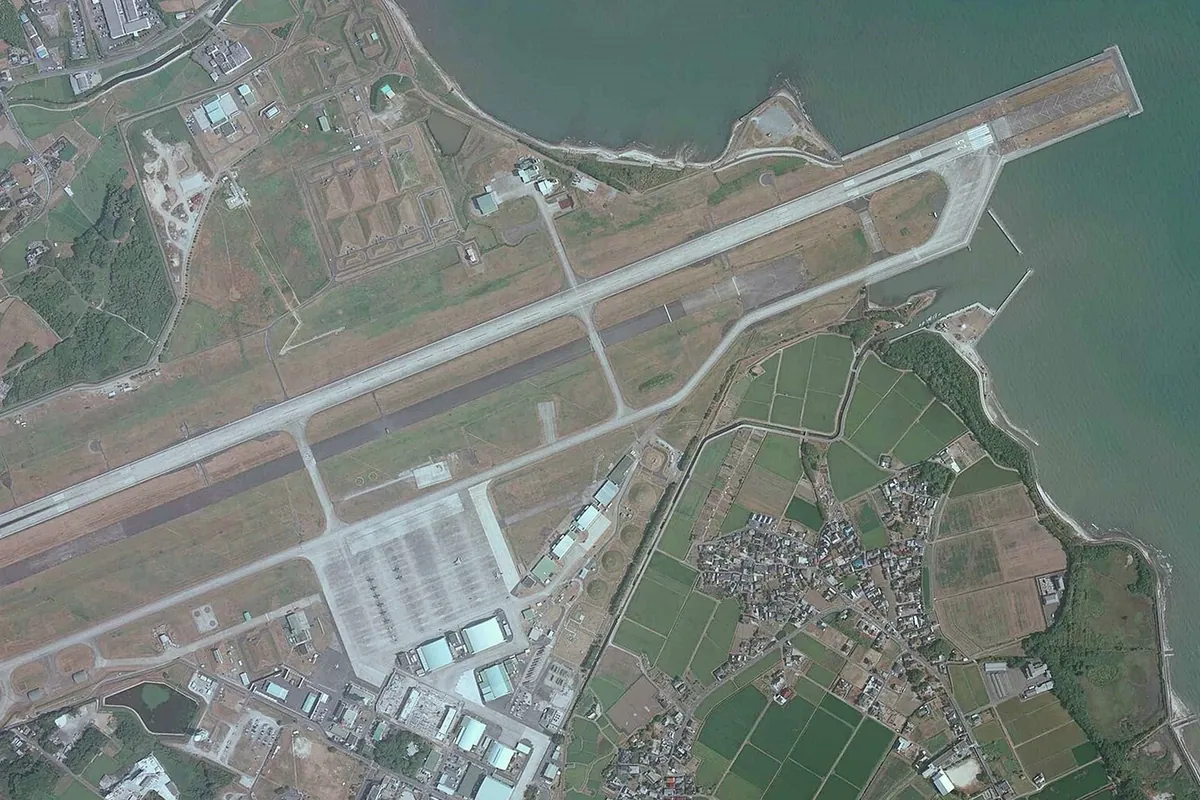海に面した滑走路とその周辺の格納庫・施設が広がる航空基地を上空から写した写真