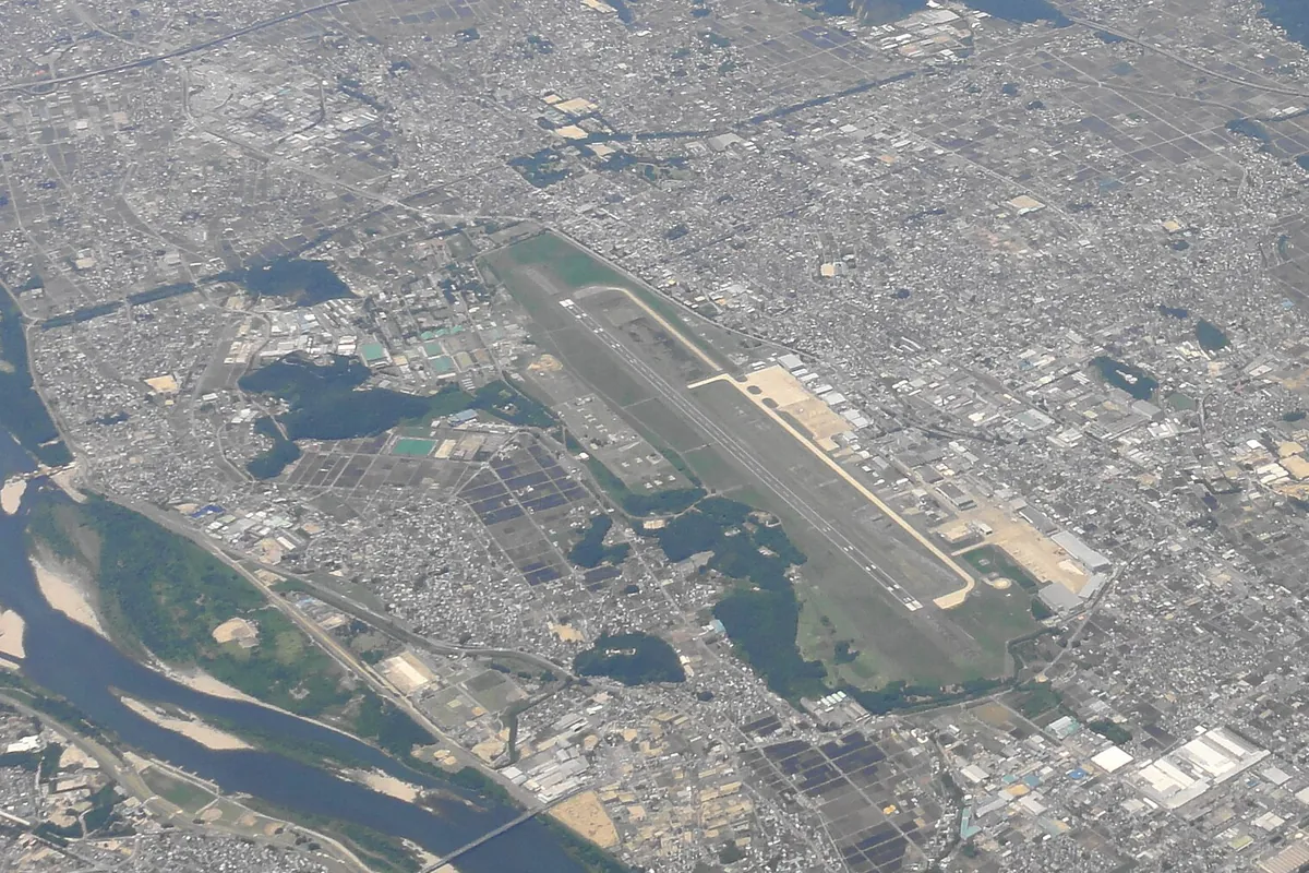 市街地の中を流れる川のそばに延びる滑走路と周辺施設を上空から写した写真