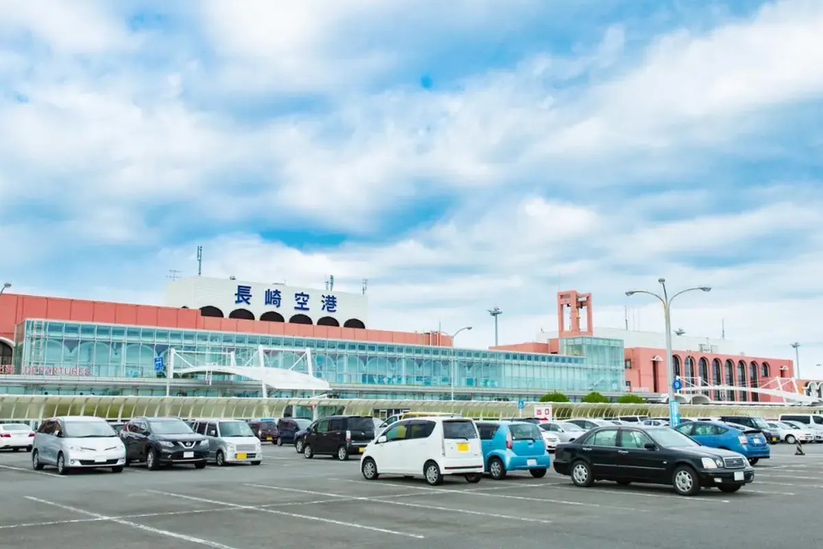 「長崎空港」と書かれた看板のあるターミナルビルの外観と、手前の駐車場に並ぶ車の写真