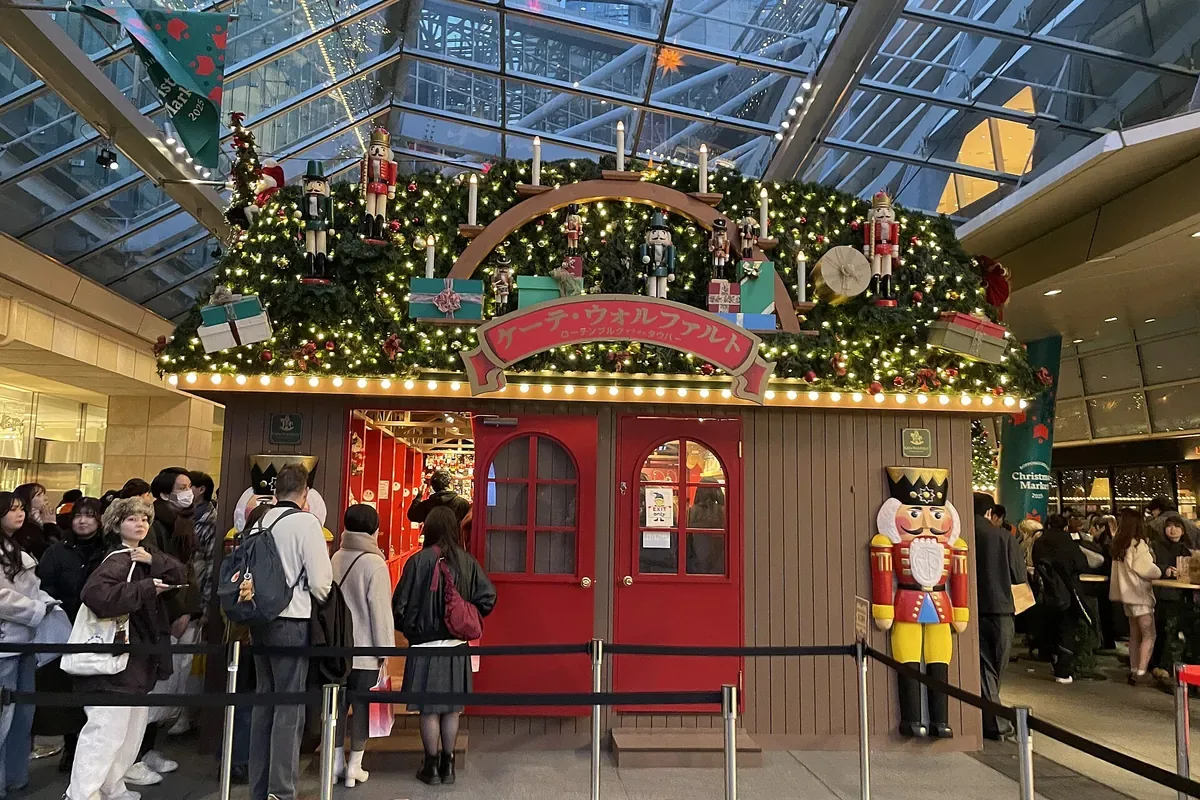 六本木ヒルズのクリスマスマーケットで、くるみ割り人形を飾った店の前に人が仕切りに沿って並んでいる写真