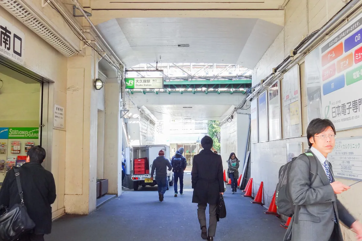 大久保駅の南口に続く構内通路で「大久保駅」の案内看板と歩く利用者が写る様子の写真