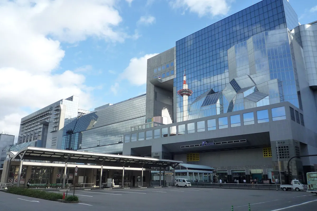 京都駅のガラス張りの駅ビルの前にバスロータリーが広がり、京都タワーがガラス面に映り込む様子の写真