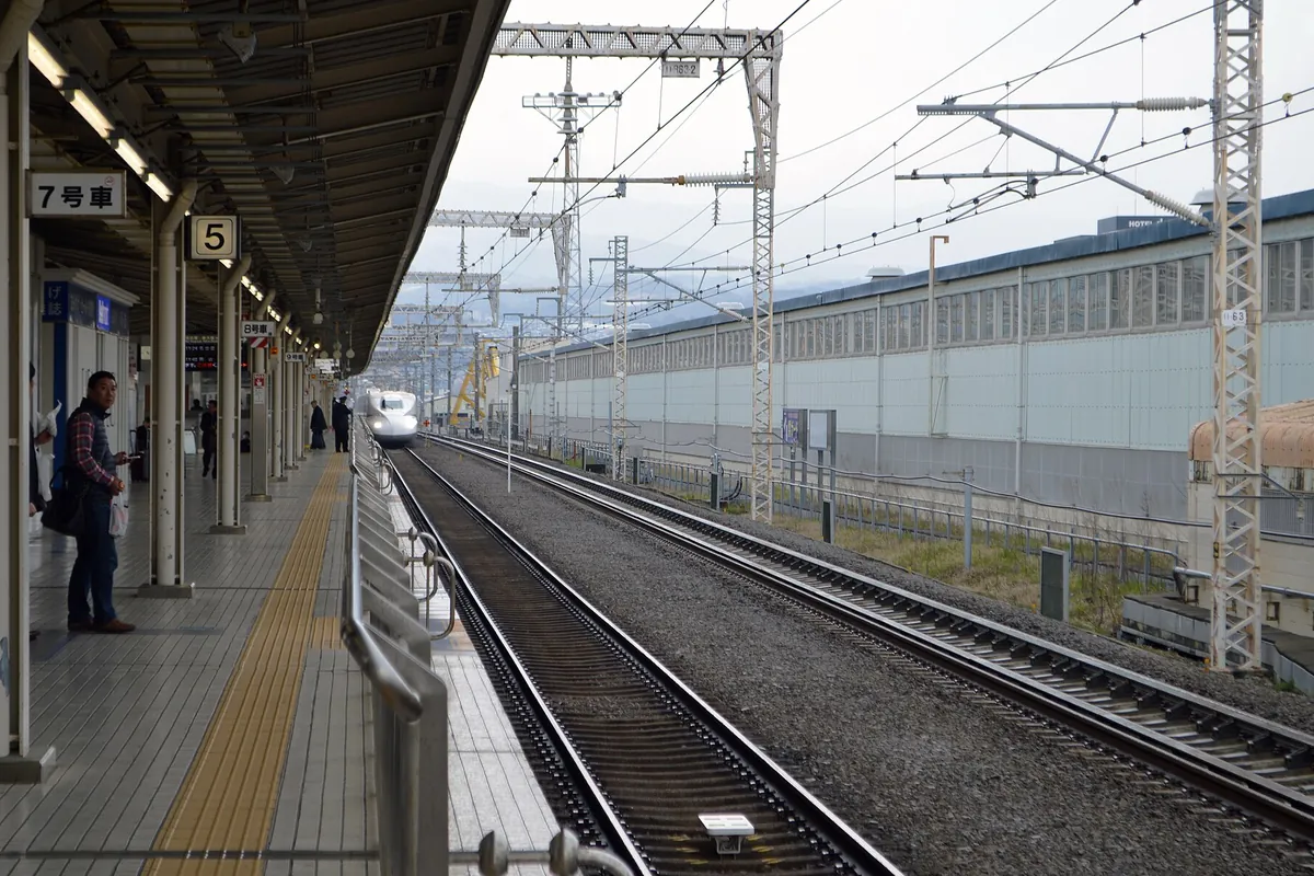 東海道新幹線の駅のホームで「7号車」と表示された番線に白い新幹線車両が入線してくる様子の写真
