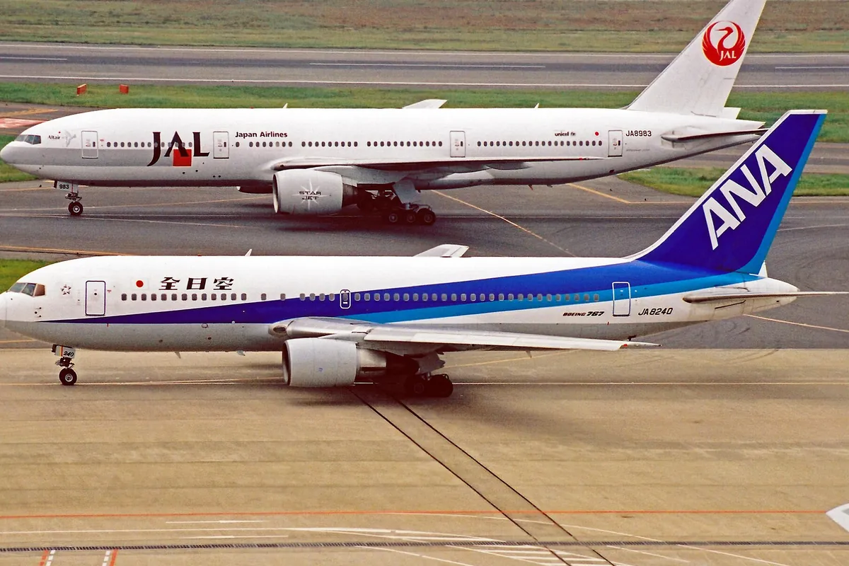 空港の駐機場で「ANA」と書かれた旅客機が手前に、「JAL」と書かれた旅客機が奥に停まっている様子の写真