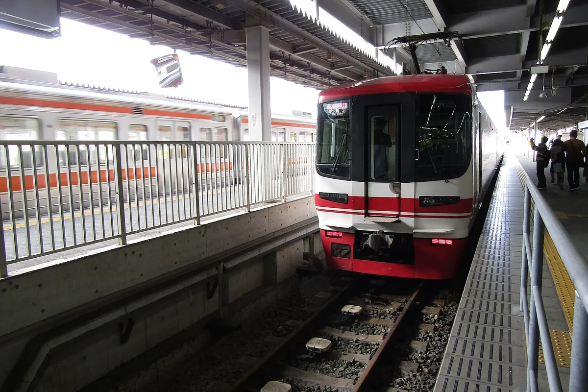 赤と白の塗装の電車がホームに停車し、隣のホームにも別の電車が走っている様子の写真