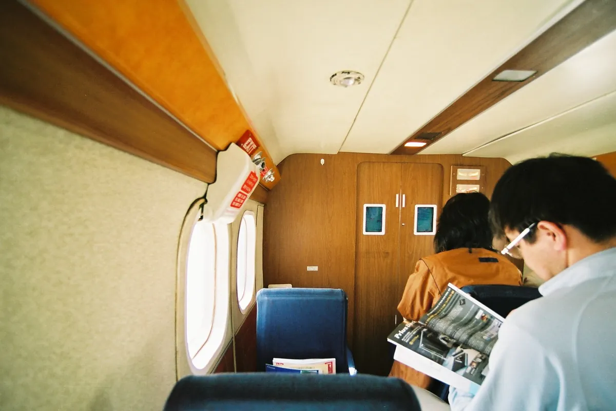 旅客機の客室内で、座席に座った乗客が雑誌を読んでいる様子の写真