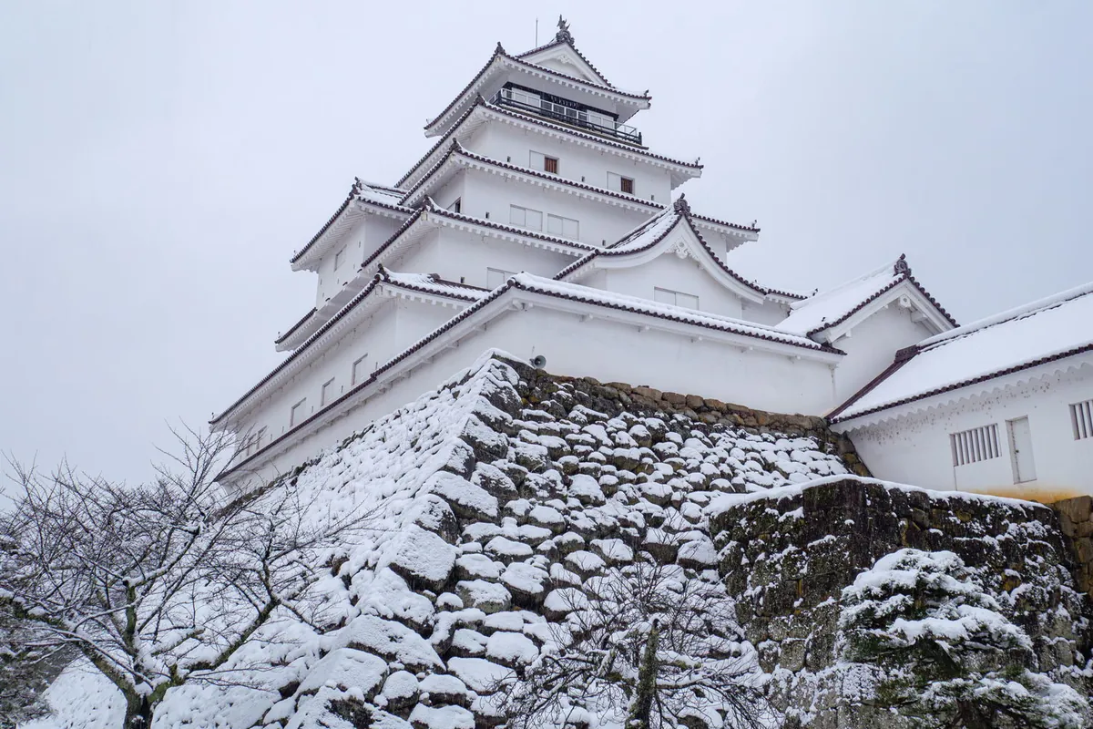 雪が積もった石垣の上に建つ会津若松市の鶴ヶ城(若松城)の白い天守閣を見上げた写真