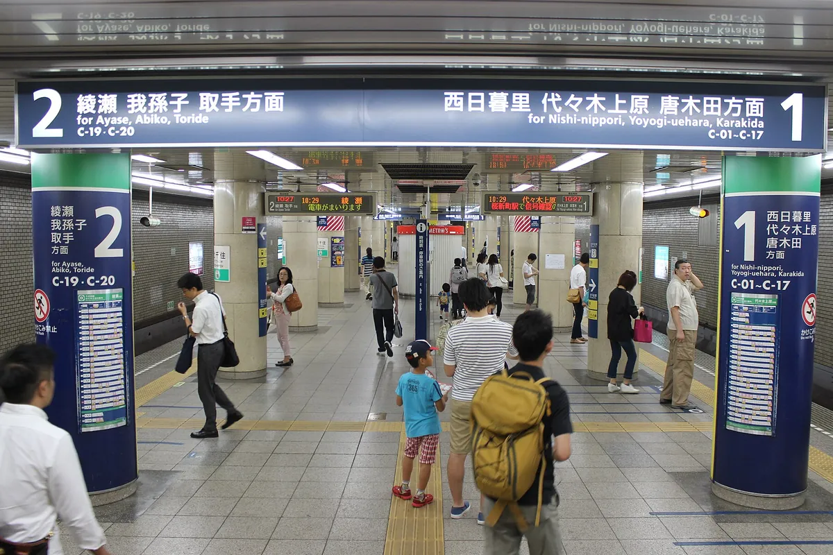 東京メトロの地下駅ホームで乗客が行き交う様子と路線案内の表示板の写真