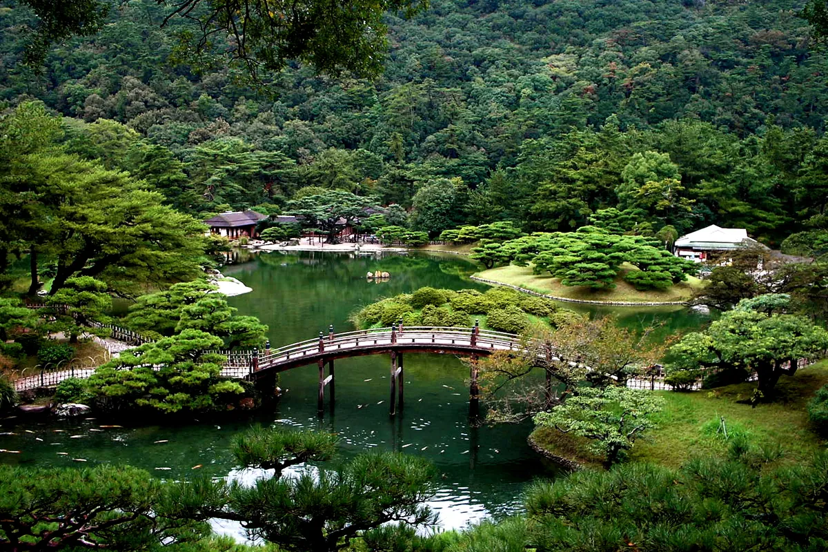 栗林公園の池に架かる太鼓橋と、周囲を囲む松や木々が茂る日本庭園の風景の写真