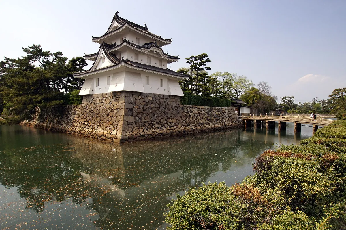 高松城跡(玉藻公園)の石垣の上に建つ白い櫓と、堀の水面に架かる橋の様子の写真