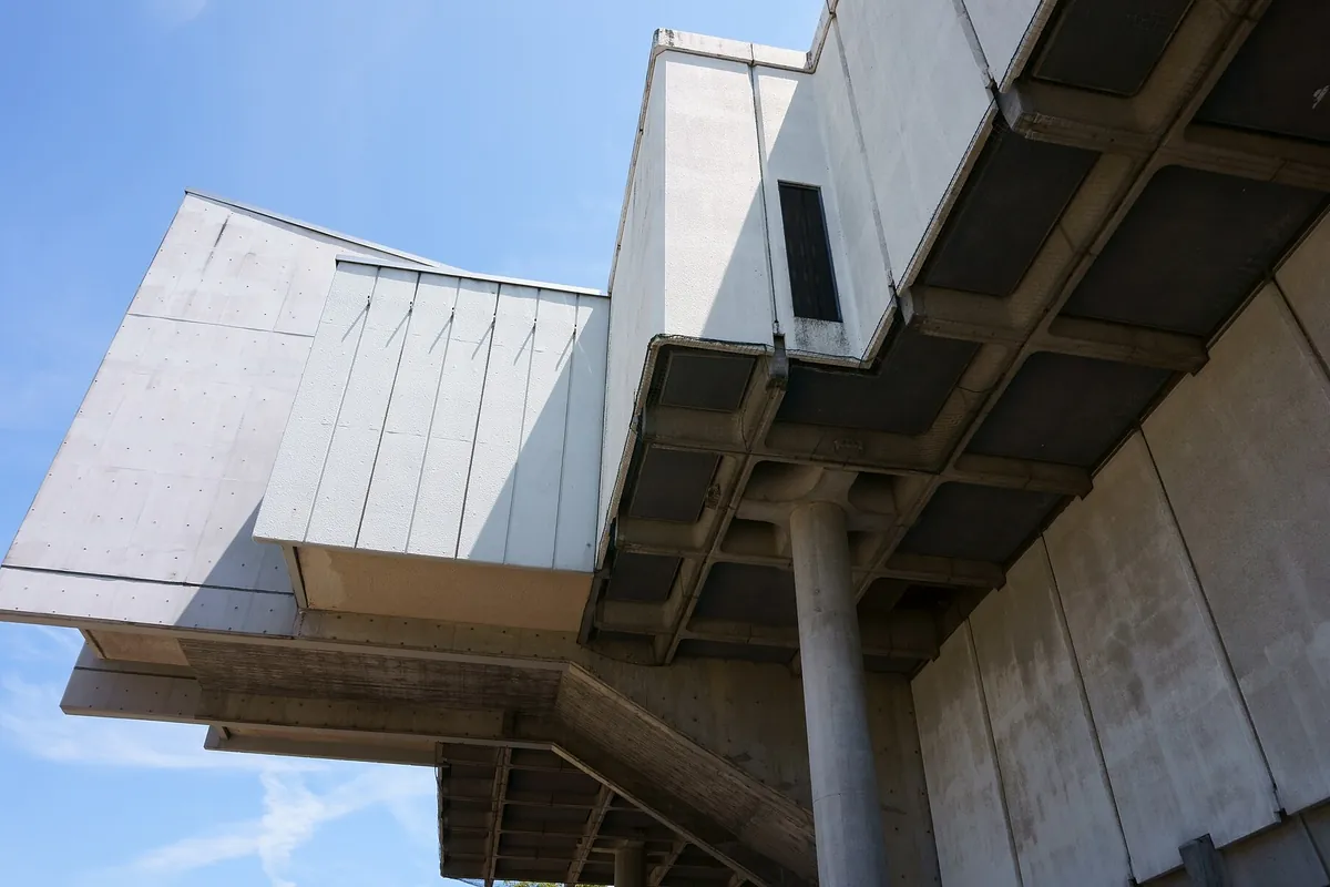 建物の軒下から見上げた、白い外壁パネルとコンクリートの梁や柱が組み合わさった屋根構造の写真