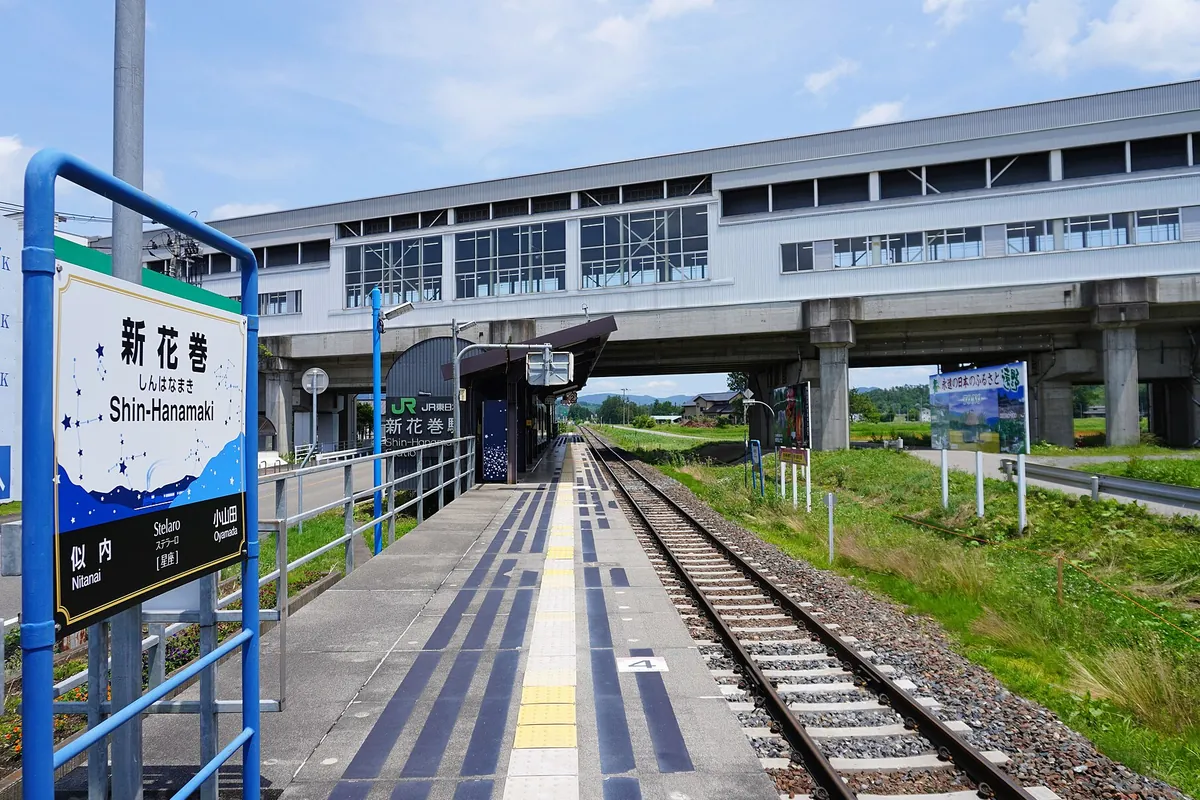 「新花巻」の駅名標が立つホームから高架の新幹線駅舎を見上げる様子の写真
