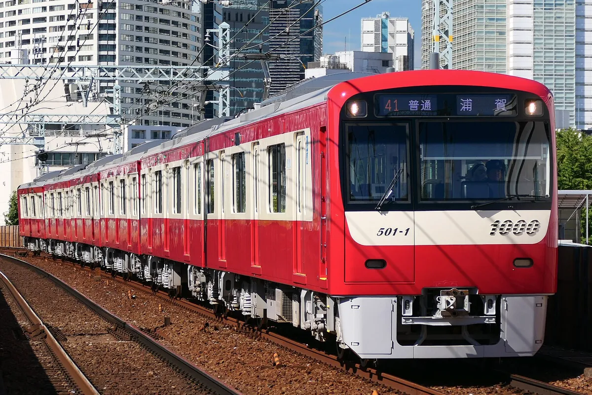 ビル群を背景に「41 普通 浦賀」の行き先表示を出した赤い電車が走行する様子の写真