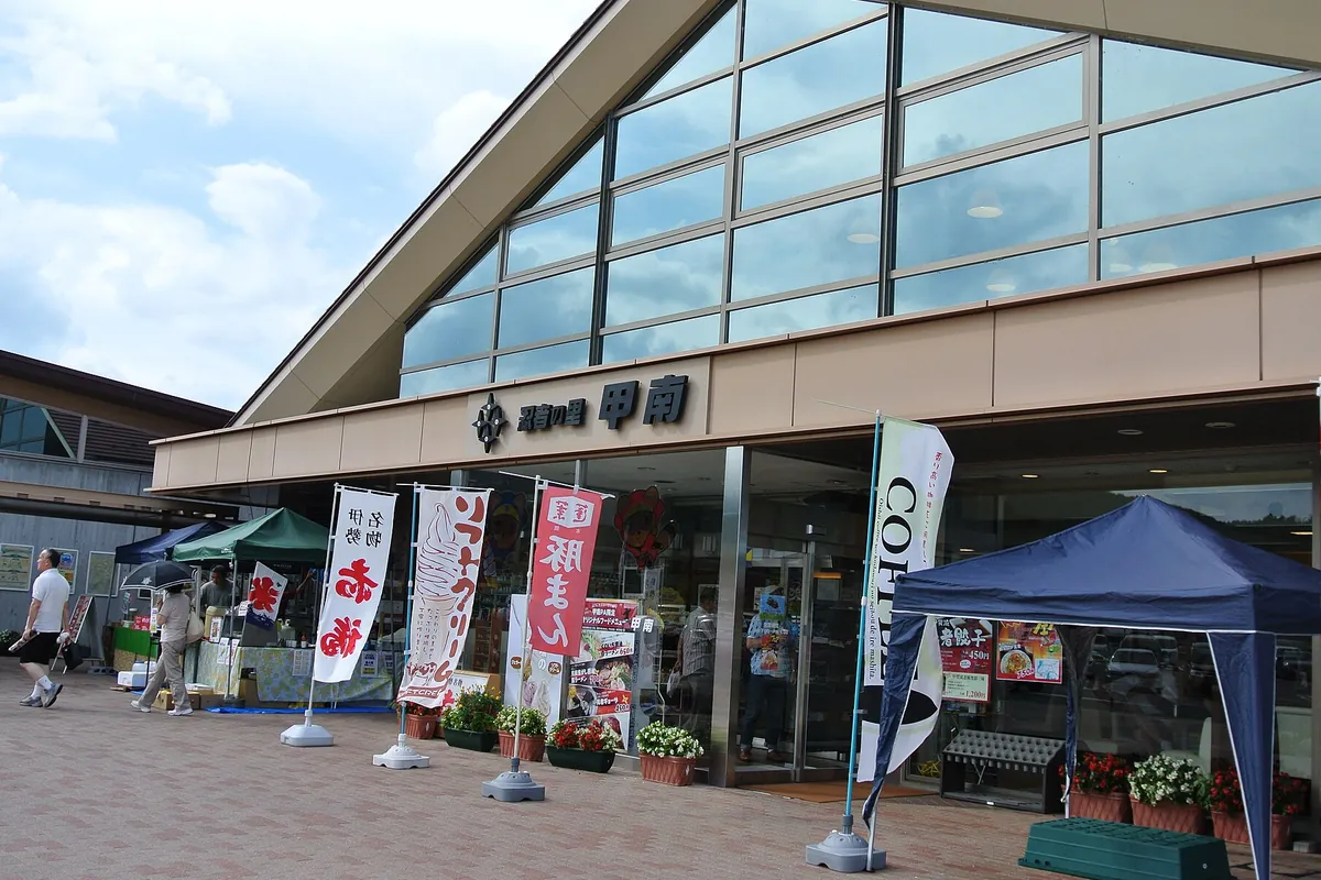 高速道路のサービスエリアの建物正面に「甲南」の看板が掲げられ、のぼりや売店が並ぶ様子の写真