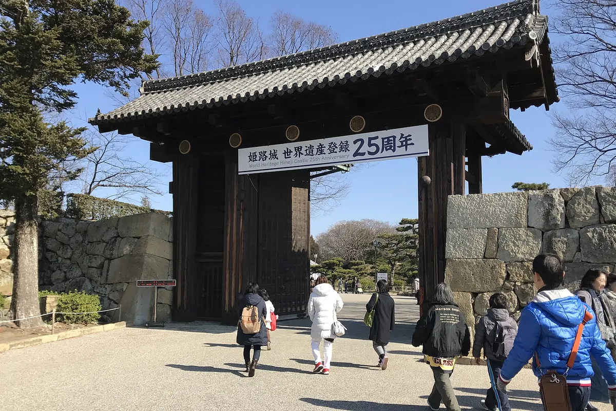 姫路城の大手門の前を観光客が歩いており、門に「姫路城 世界遺産登録25周年」の横断幕が掲げられている写真