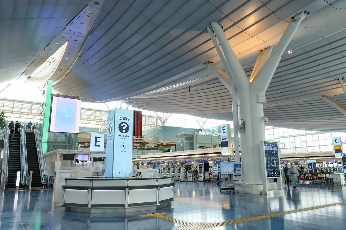 空港ターミナルの出発ロビーで、案内カウンターやチェックイン機、フライト案内表示が並ぶ様子の写真