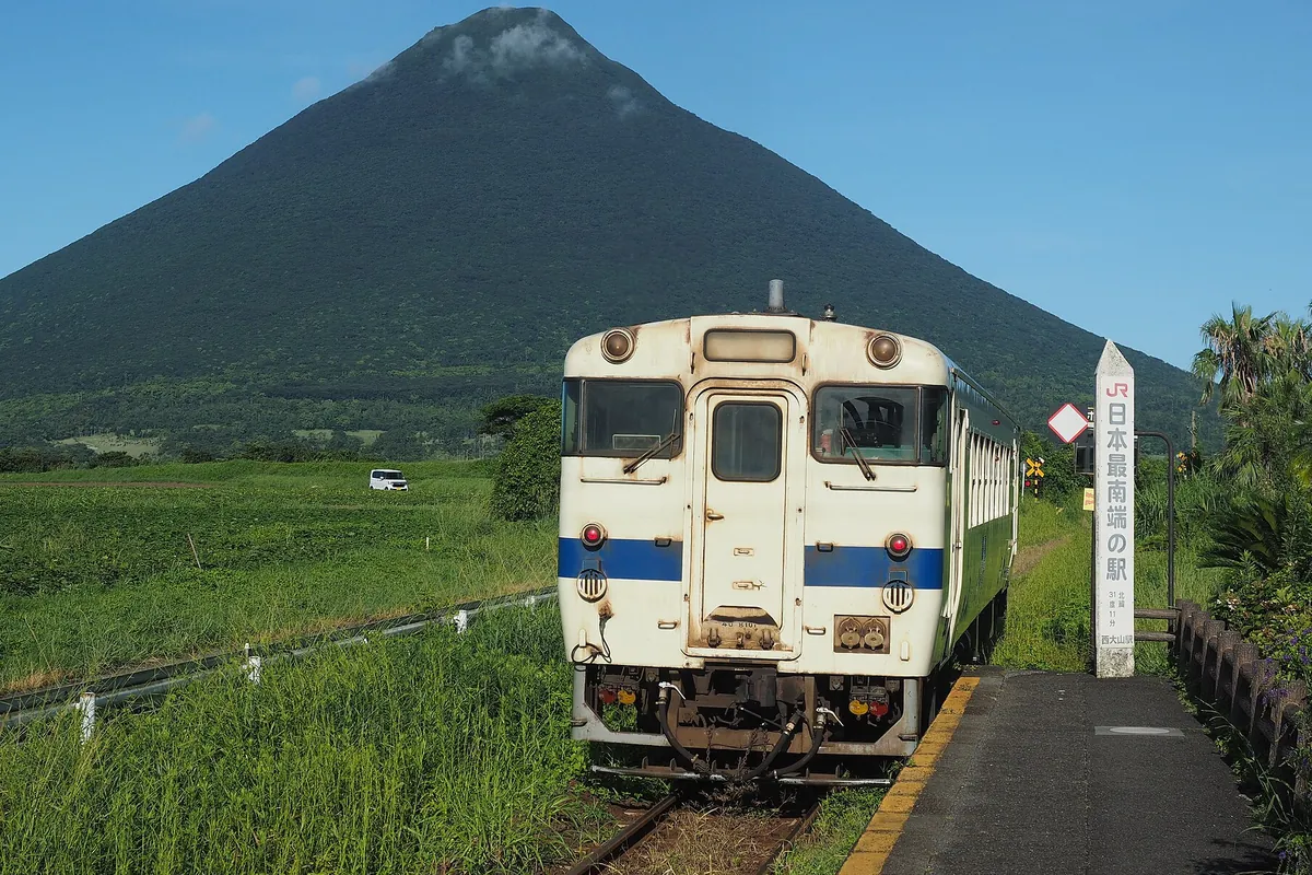 開聞岳を背景に西大山駅のホームに停車するディーゼル列車と「日本最南端の駅」の駅名標の写真