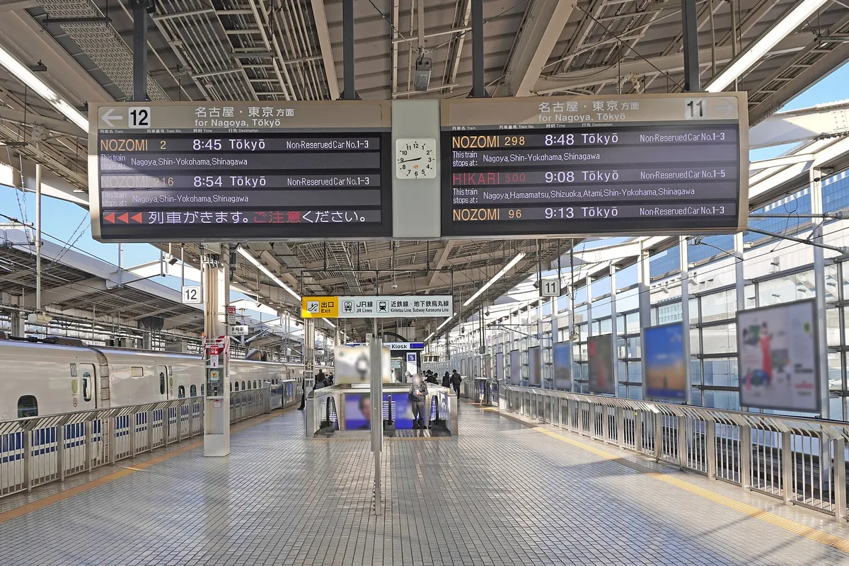 京都駅の新幹線ホームで、名古屋・東京方面の発車案内板とホームに停車する新幹線車両が写る写真