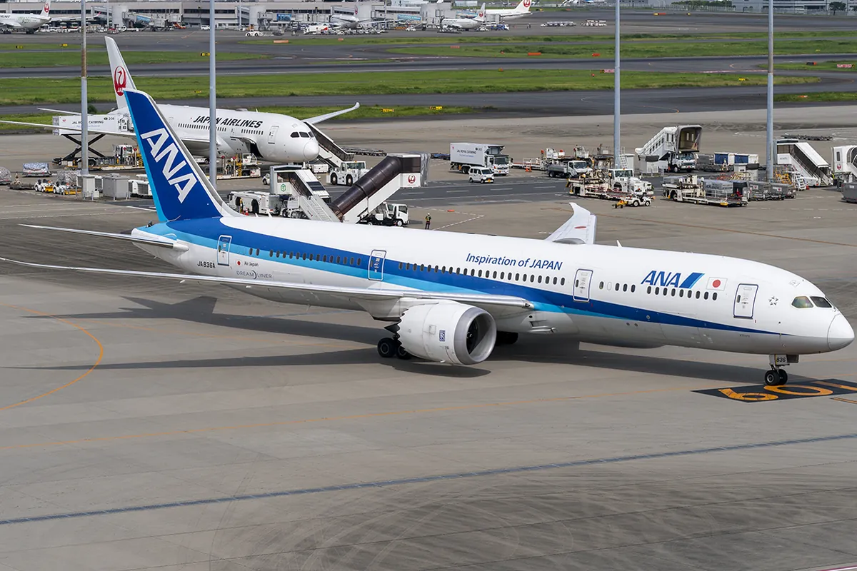 空港の駐機場でANAのボーイング787-9が走行し、奥にJAL機が駐機している様子の写真