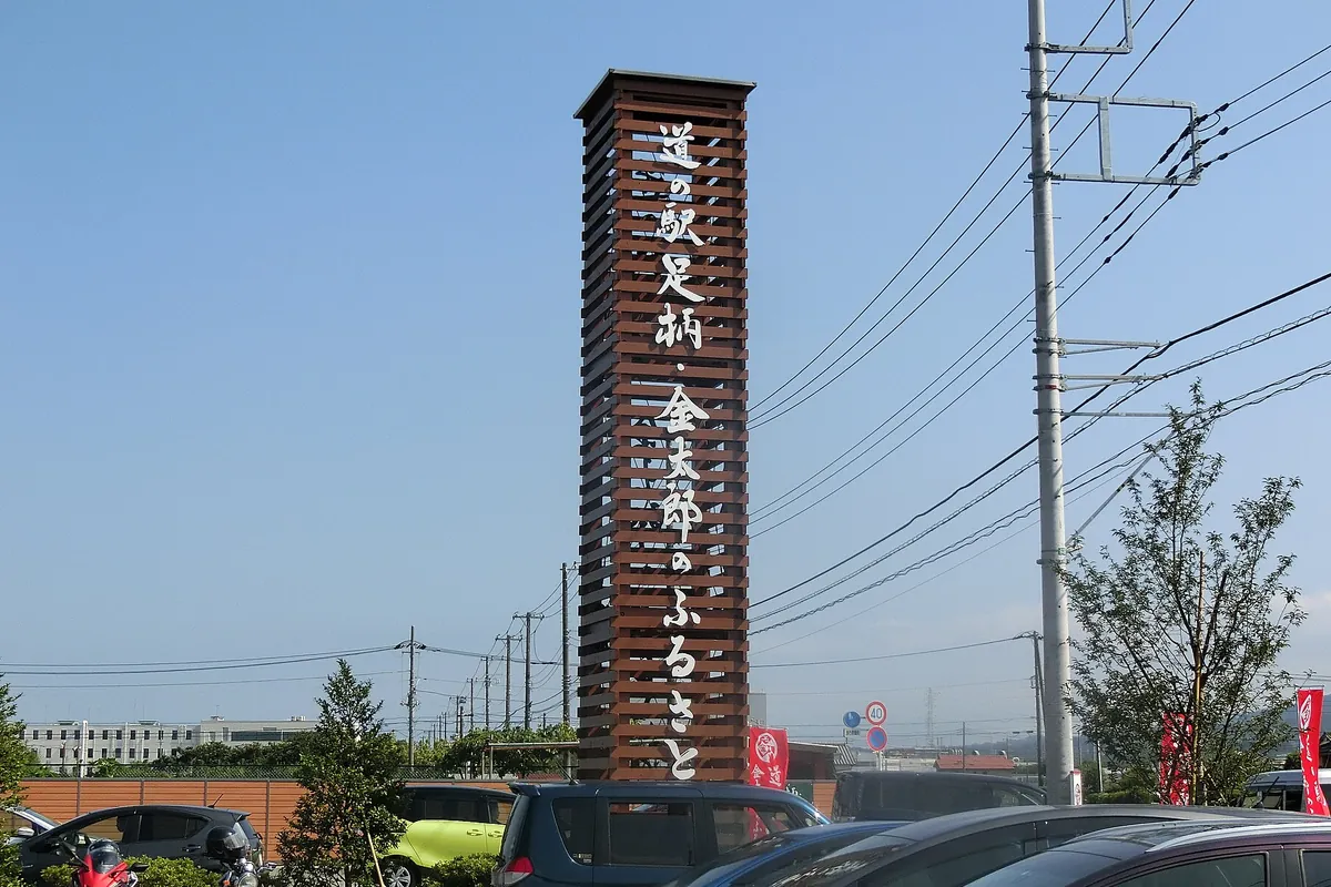 「道の駅足柄・金太郎のふるさと」と書かれた木製の大きな看板塔が駐車場の奥にそびえ立つ様子の写真