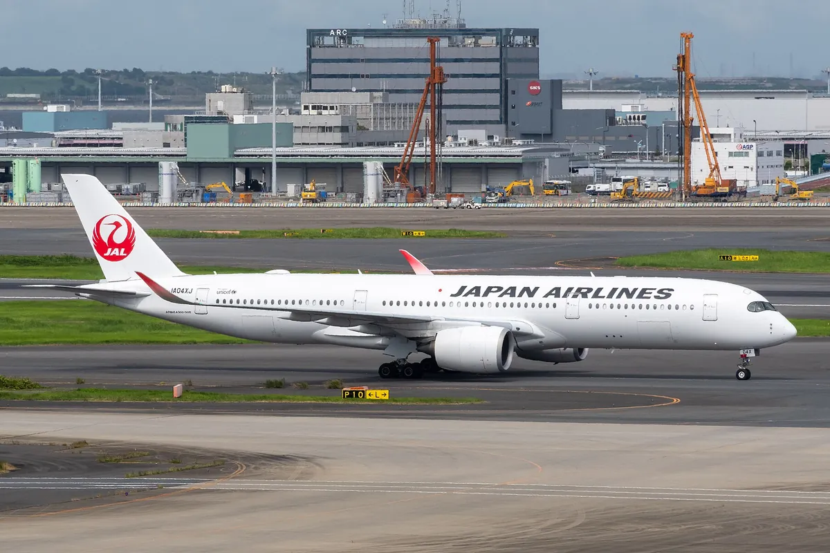 空港の誘導路でJAPAN AIRLINESの機体ロゴが入った白いエアバス機が走行している写真