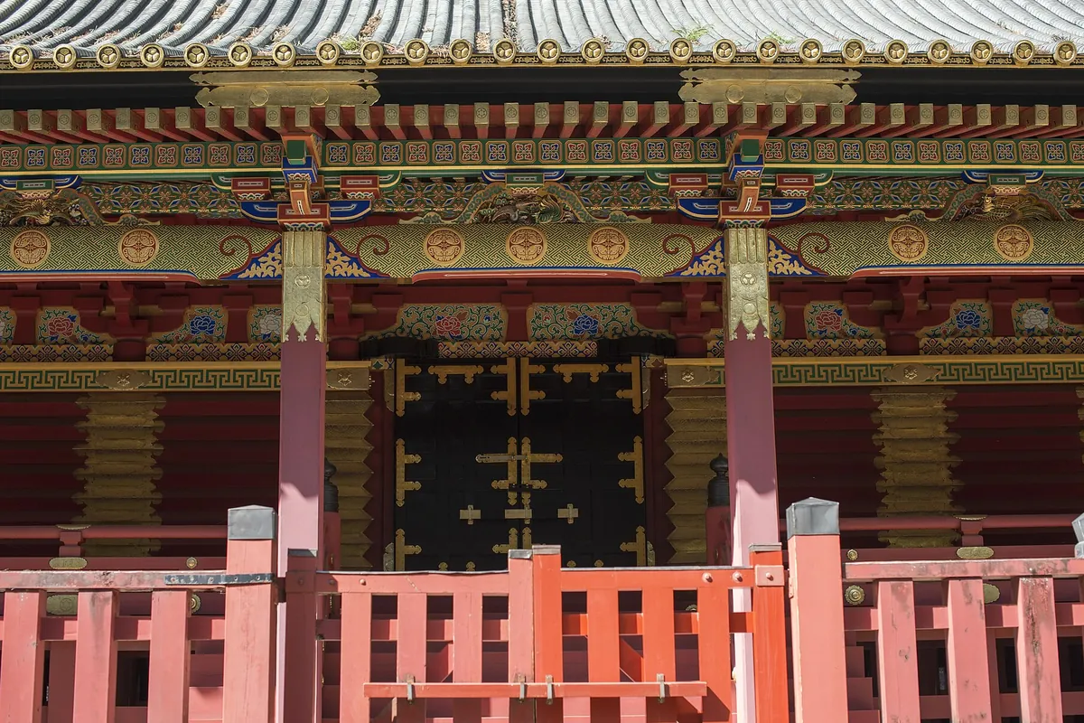 朱色の欄干越しに、金色の彫刻と黒塗りの扉で飾られた社殿の軒先を見上げた写真