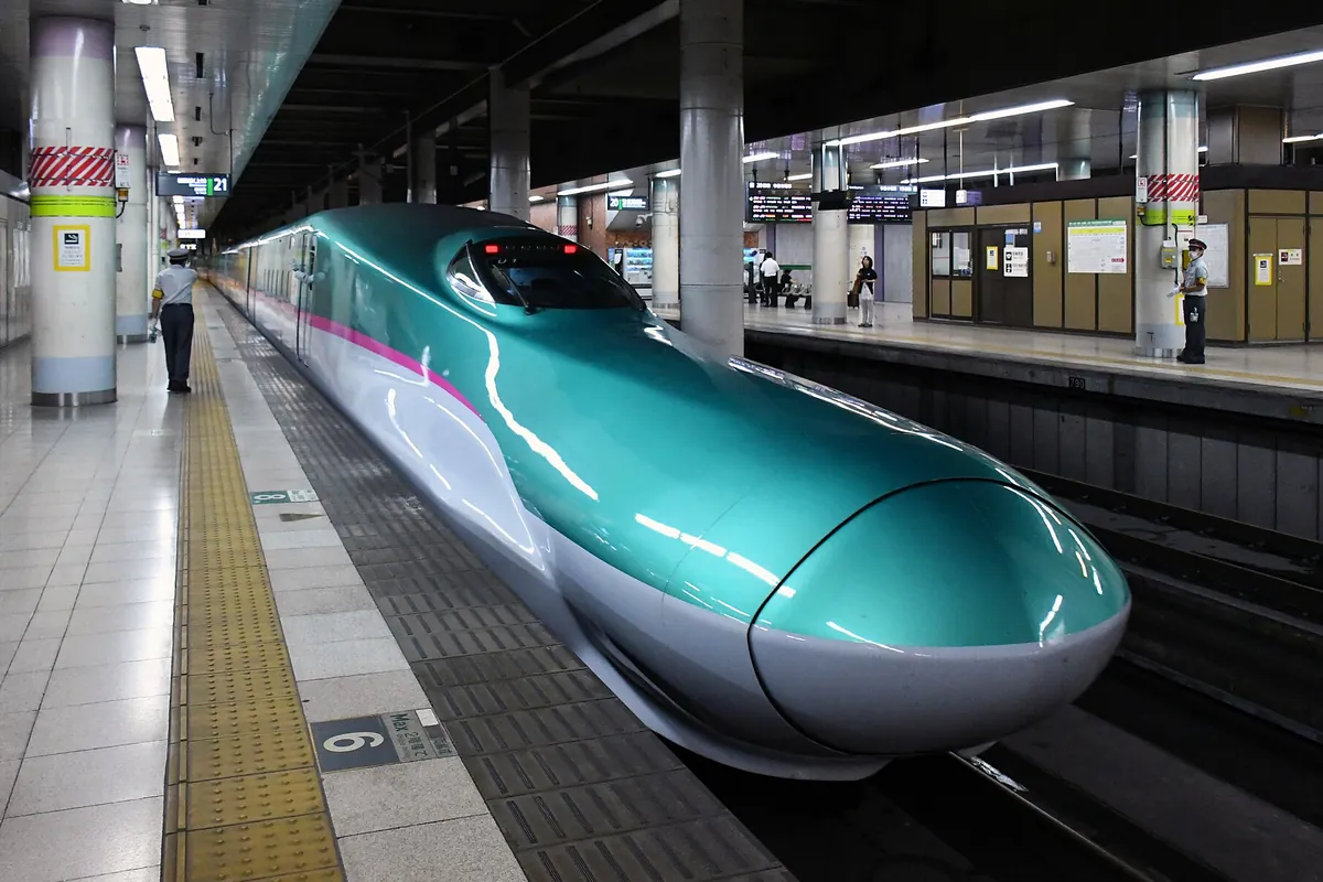 新幹線の駅のホームで、緑と白の車体にピンクの帯が入った東北新幹線E5系が停車している写真