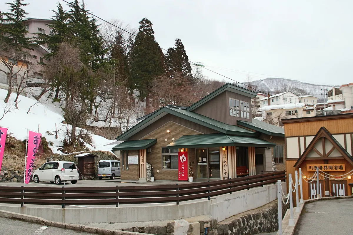 雪が残る山あいの温泉街で、緑屋根の建物や『川原湯共同浴場』の看板が並ぶ通りの写真