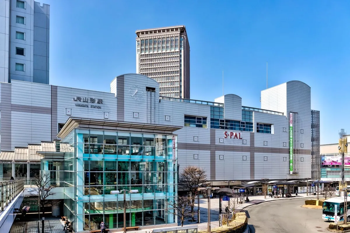 「JR山形駅」の駅舎と商業施設「S-PAL」が併設された外観、青空の下にロータリーとバスが見える写真