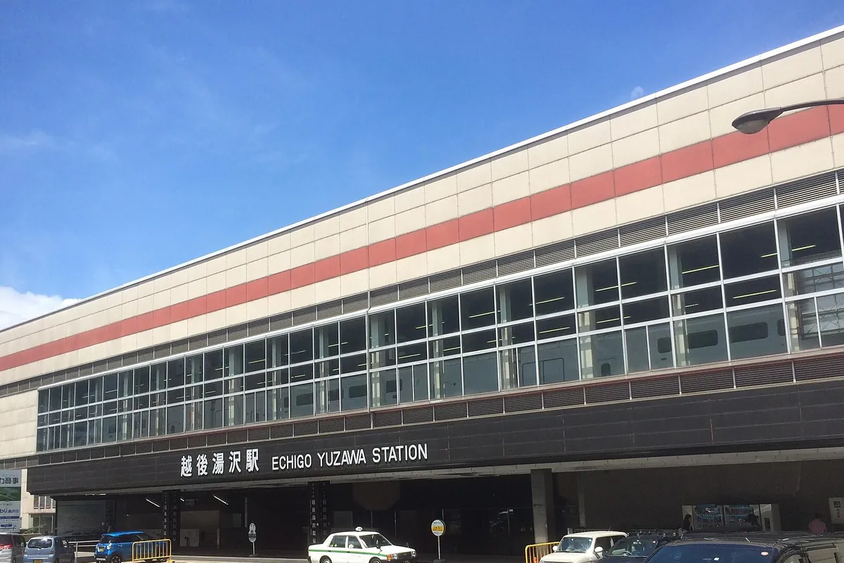 越後湯沢駅の駅舎正面に「越後湯沢駅 ECHIGO YUZAWA STATION」の看板が掲げられ、駅前にタクシーや車が停まっている様子の写真