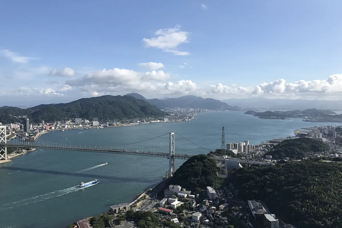 高所から見下ろした関門橋と関門海峡、両岸の街並みと船の様子の写真