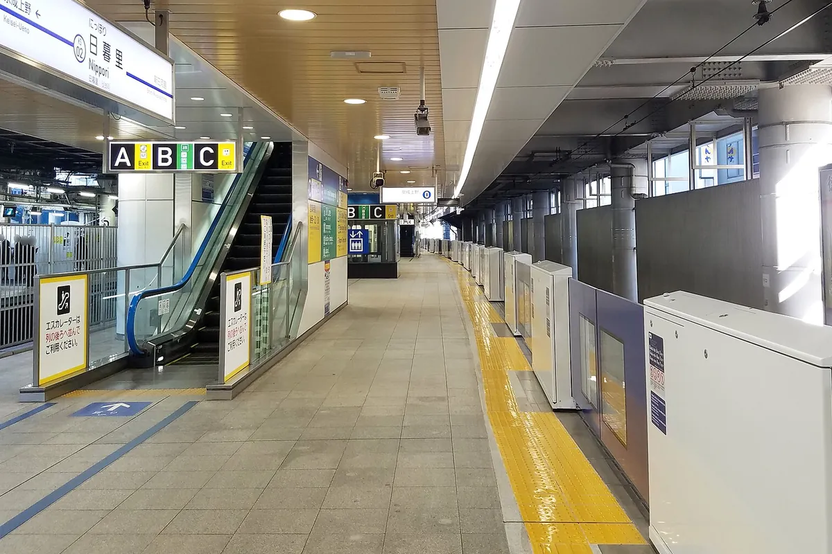 「日暮里 Nippori」の駅名標が掲げられたホームで、エスカレーターと出口案内A・B・Cが並ぶ様子の写真
