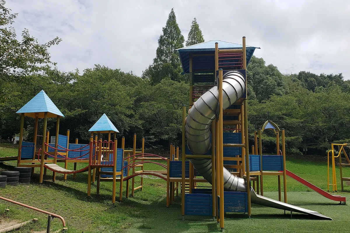 公園の芝生広場に設置された大型複合遊具で、らせん状のチューブすべり台とよじ登り用の通路が組み合わさった様子の写真