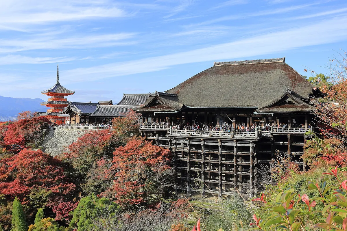 紅葉に囲まれた清水寺の本堂と、舞台造りの懸造りに多くの参拝者が立つ様子の写真