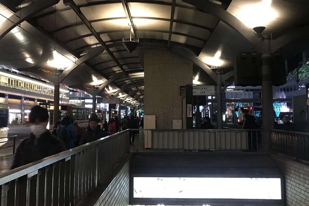 夜の京都駅前のバスターミナルで、停車する複数のバスと行き交う利用者の様子の写真