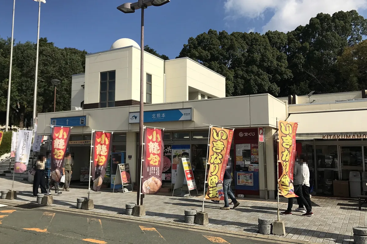 九州自動車道・北熊本サービスエリアの建物外観で、「北熊本」の案内看板と小龍包やいきなり団子の幟が並ぶ様子の写真