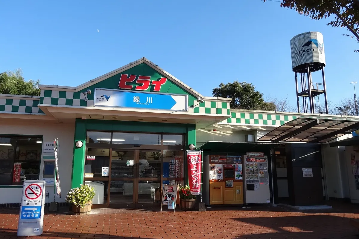 九州自動車道・緑川パーキングエリアの売店「ヒライ」の入口外観で、緑と白の市松模様の屋根と給水塔が写る様子の写真